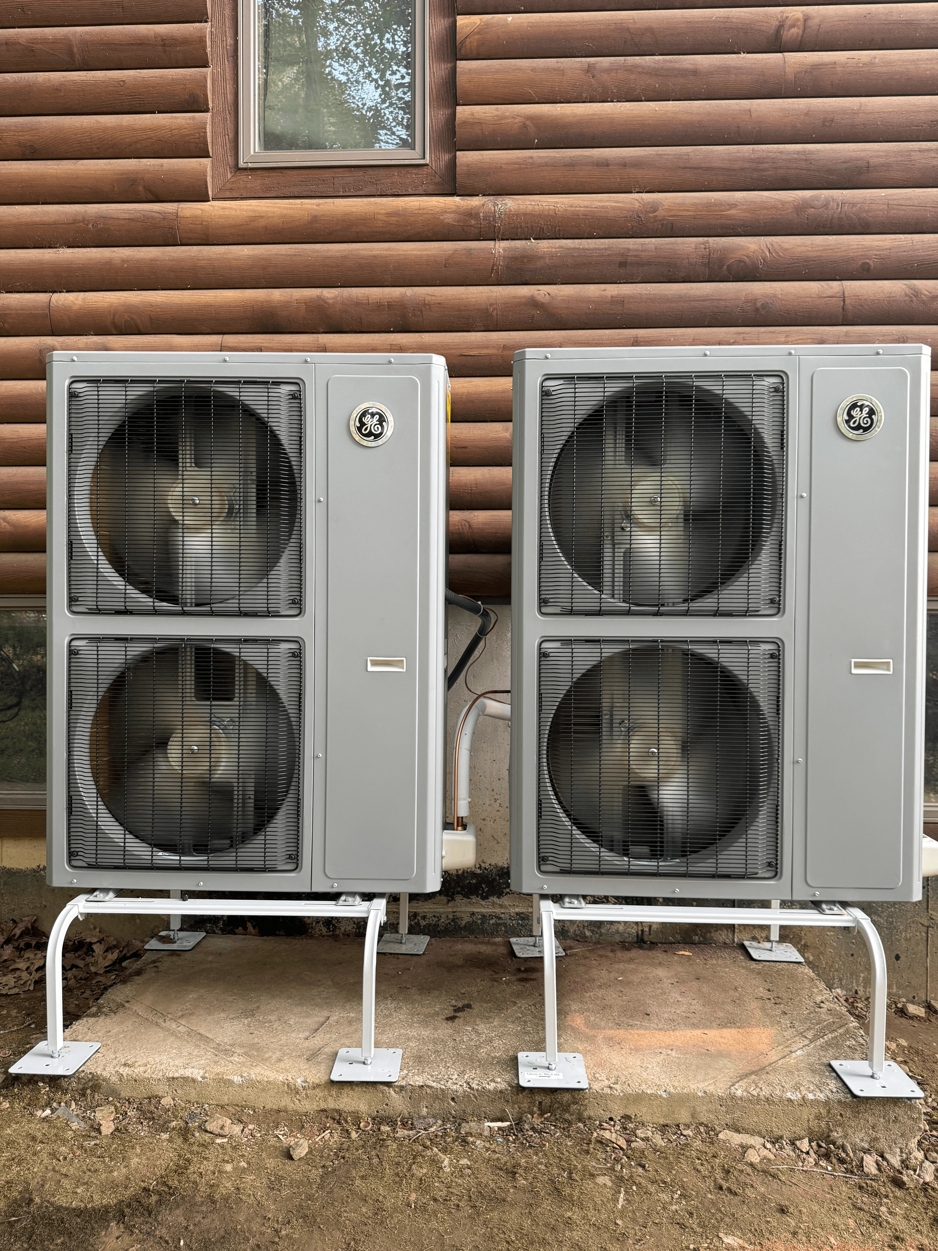 Dual GE heat pump condenser units installed at log cabin exterior
